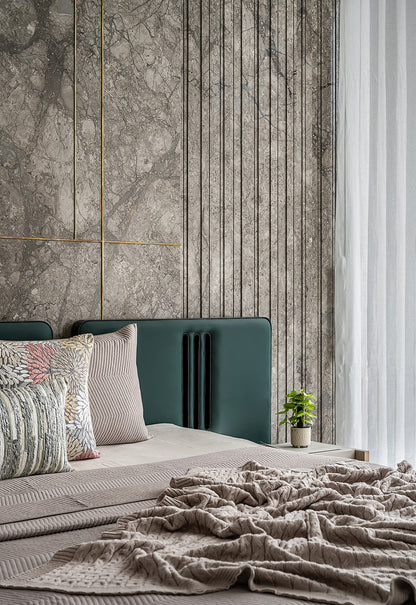 Modern living room with a green sofa, decorative pillows, and a side table against a marble wall.