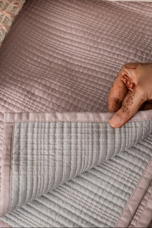 Textured fabric swatch held by a hand with a patterned pillow in the background